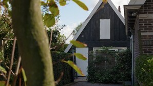 A modern house with a dark wooden exterior, a white door, and a brick wall with the number 11. - Holiday Home Near Lawn Bowling in Krabbendam (Warmenhuizen)