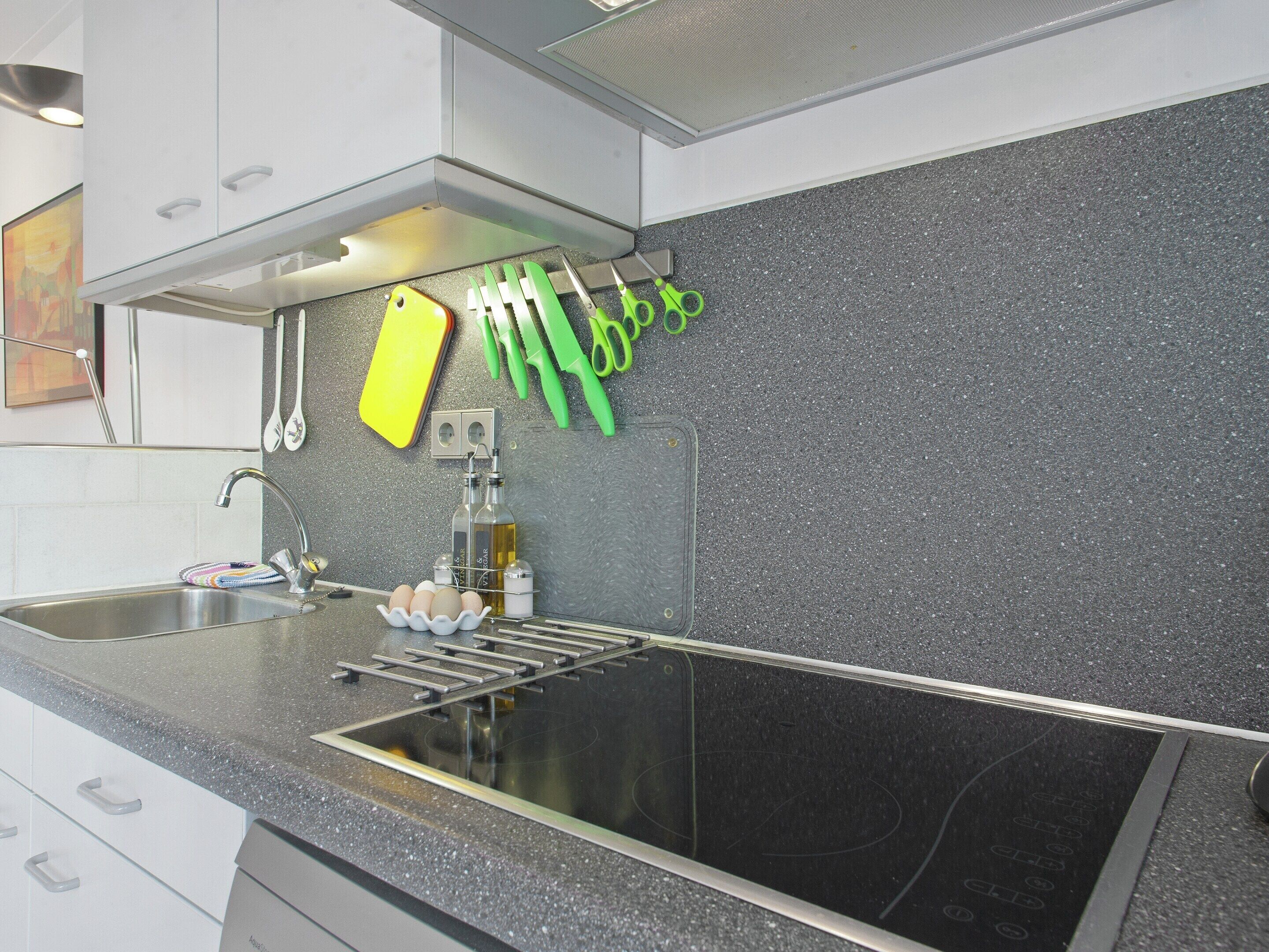 Une cuisine avec une plaque de cuisson noire, un évier et divers ustensiles de cuisine suspendus au-dessus.