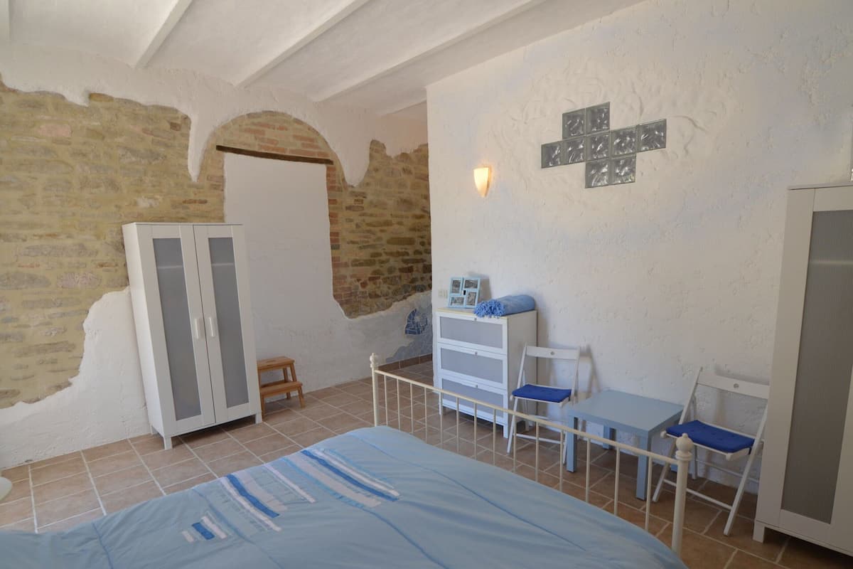 A bedroom with a bed, a dresser, a desk with chairs, and a cross-shaped wall decoration.