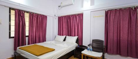 A hotel room with a single bed, a small table with a chair, and a water bottle on the table.