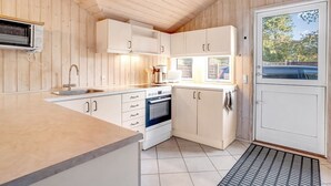 A compact kitchen with wooden walls, a built-in oven, a sink, and a clock on the wall.