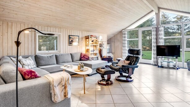 A spacious living room with a large sofa, a coffee table, and two chairs. There is a television and a bookshelf in the room.