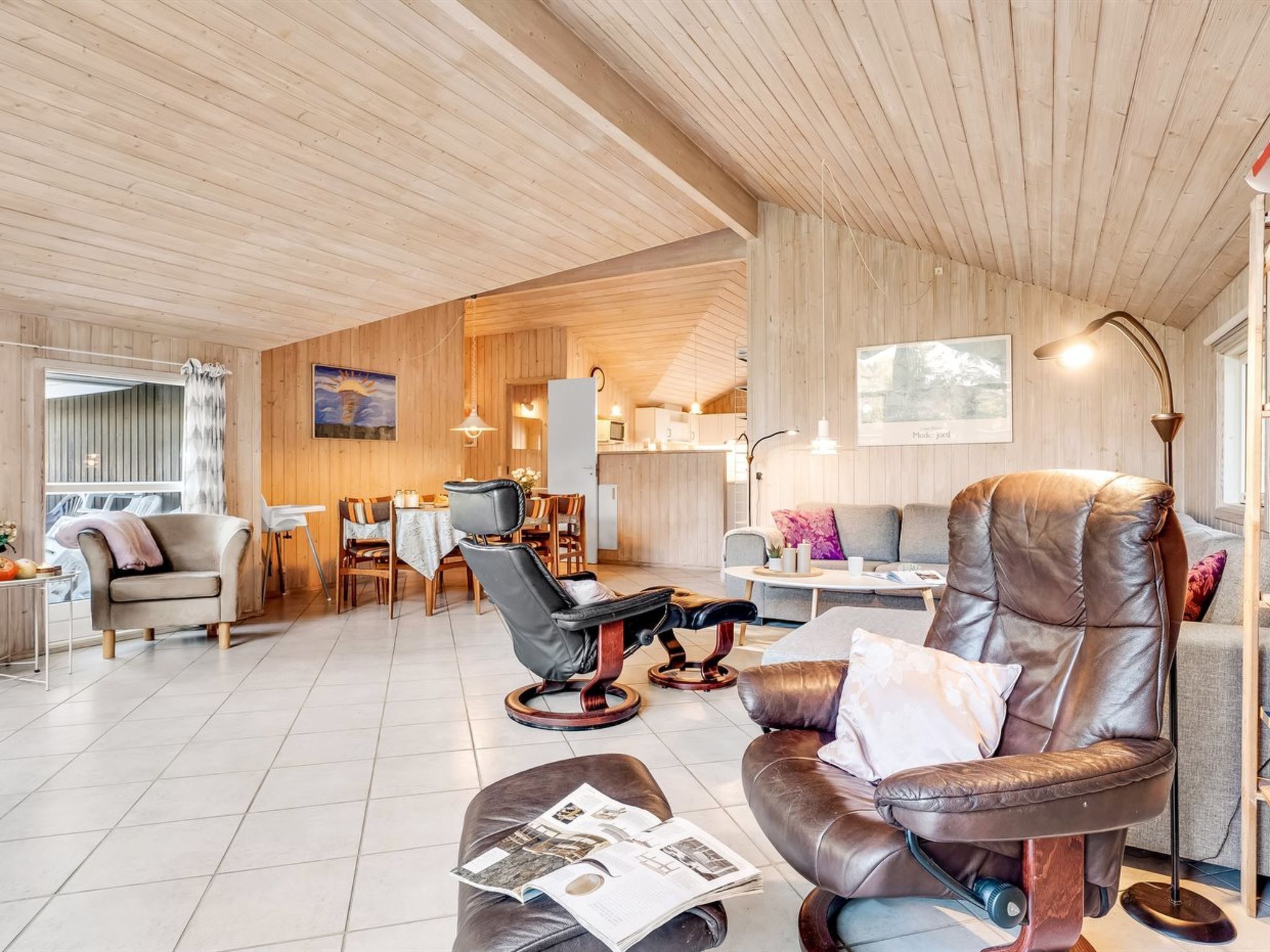 A modern living room with a leather sofa, a dining area, and a kitchen in the background.