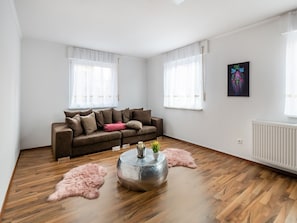 Un salon moderne avec un canapé marron, des rideaux blancs, une table basse ronde et un tapis moelleux.