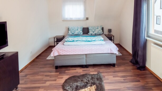 A bedroom with a bed, bedside tables, a TV, and a window with curtains. - Holiday Home in Mahlberg in the Ortenau District (Mahlberg)