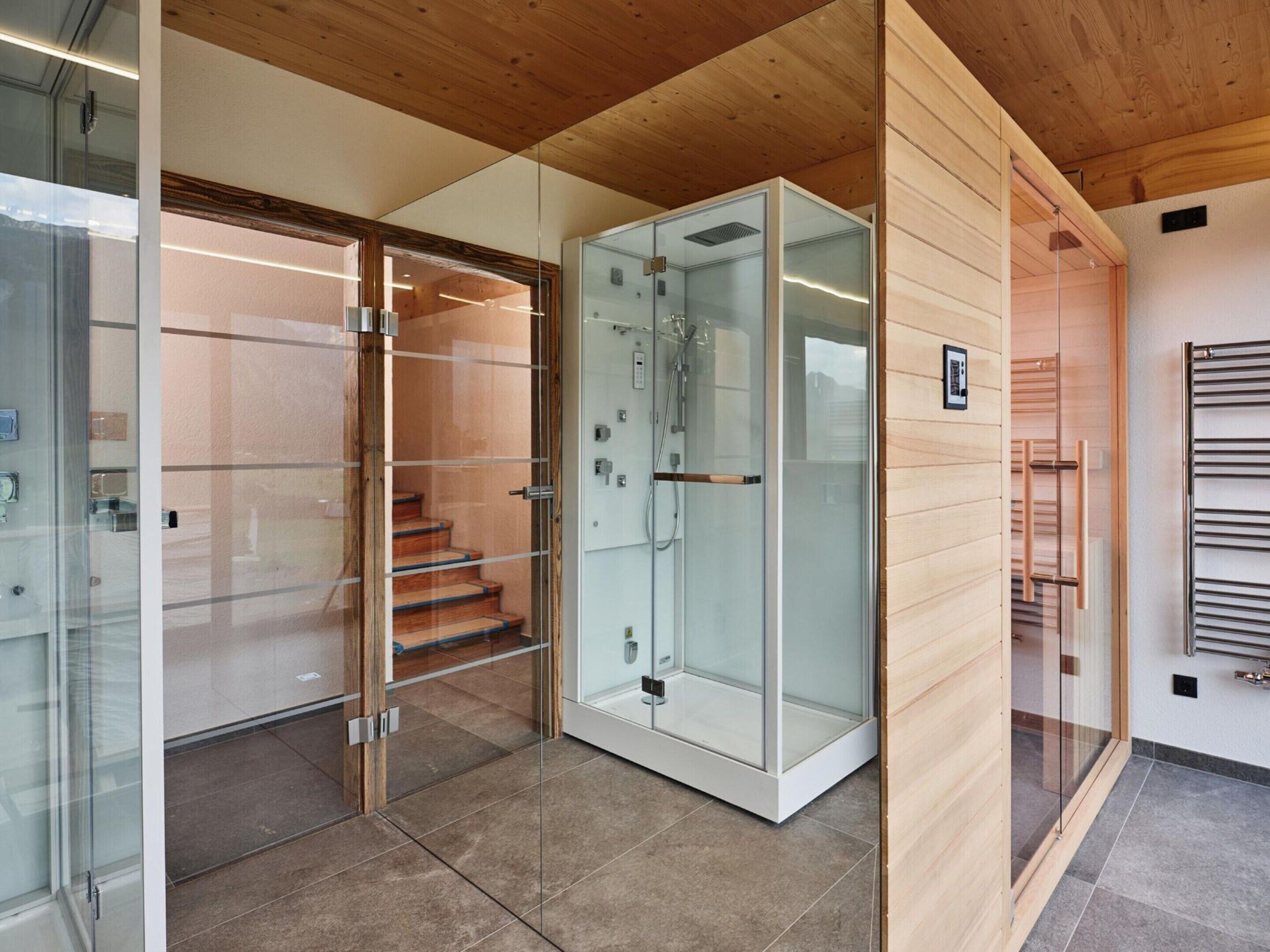 A modern bathroom with a glass shower enclosure, wooden flooring, and a visible towel rack.