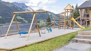 A playground with swings and slides, set against a backdrop of mountains and a clear sky. - Majestic Chalet With Pool and Sauna (Haus)