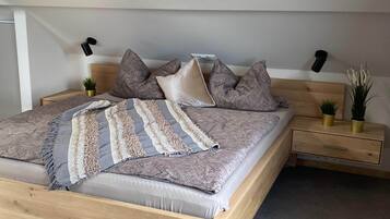 A neatly made bed with patterned bedding, a bedside table with a lamp, and two small potted plants.
