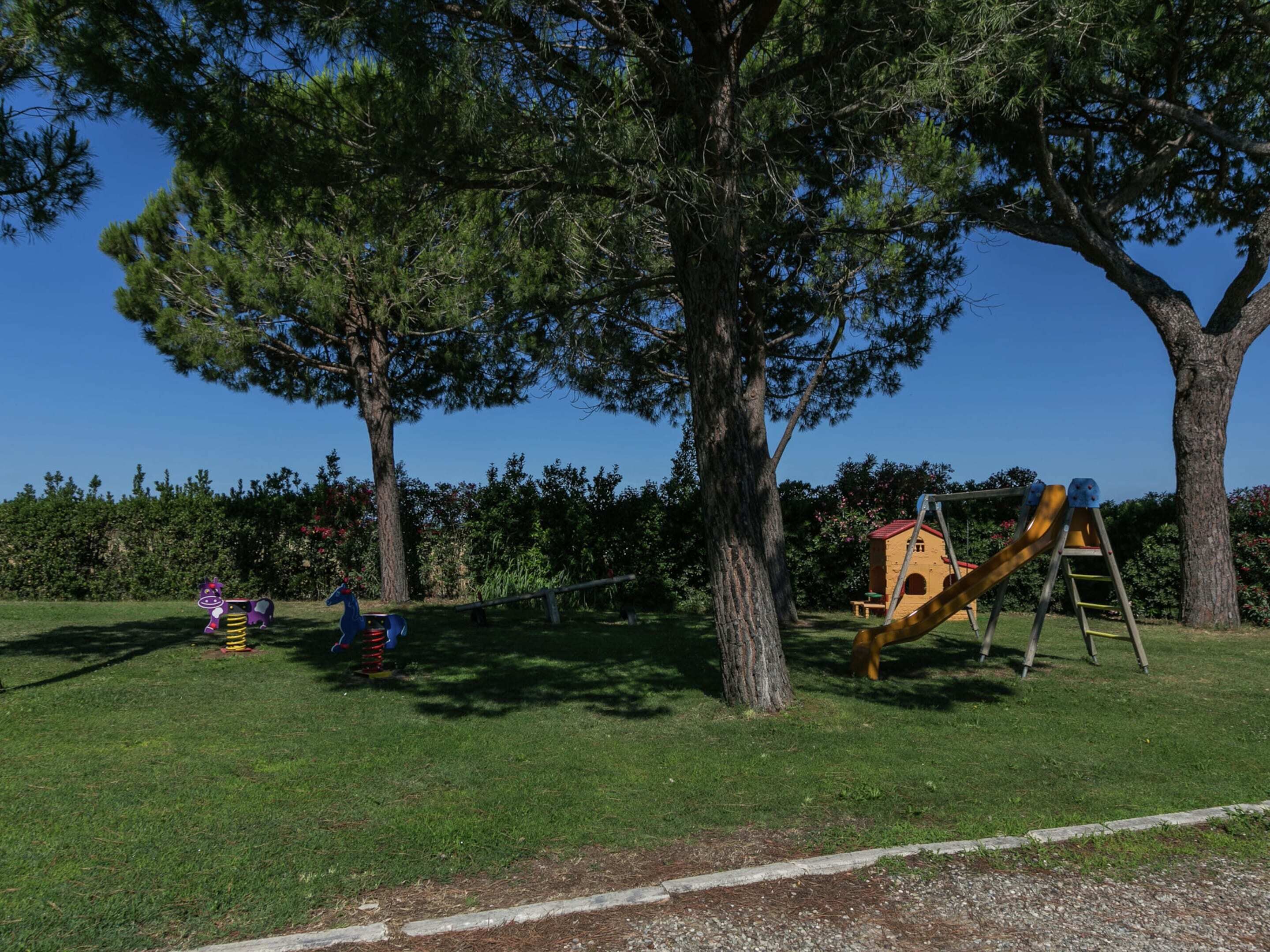 Un parque infantil con tobogán y columpios, rodeado de árboles y césped.