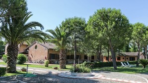 A courtyard with palm trees, a brick building, and a gravel path. - Appealing Apartment Just 7 km From the Beach (Grosseto)