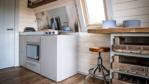 A compact kitchen with a washing machine, a small dining area, and a stool. - Rutland Rural Retreats - Woodpecker pod
 (Esher)
