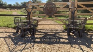 A wooden gate with a metal emblem, two metal carts, and a gravel path. - Rutland Rural Retreats - Woodpecker pod
 (Esher)