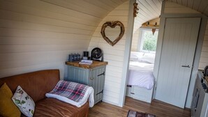 A cozy room with a brown leather sofa, a small wooden cabinet, and a heart-shaped decoration on the wall. - Rutland Rural Retreats - Woodpecker pod
 (Esher)