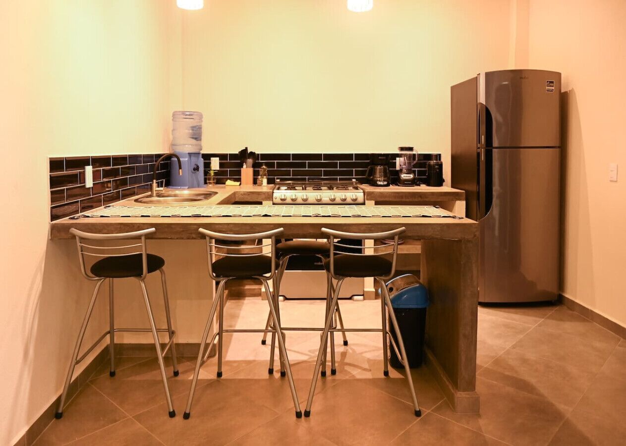 Een compacte keuken met een centraal eiland, vier barkrukken, een roestvrijstalen koelkast en een waterdispenser.