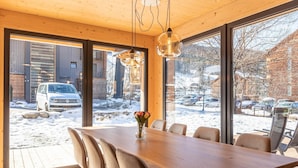 Ein moderner Essbereich mit Holztisch und -stühlen, großen Fenstern und Blick auf eine verschneite Landschaft.
