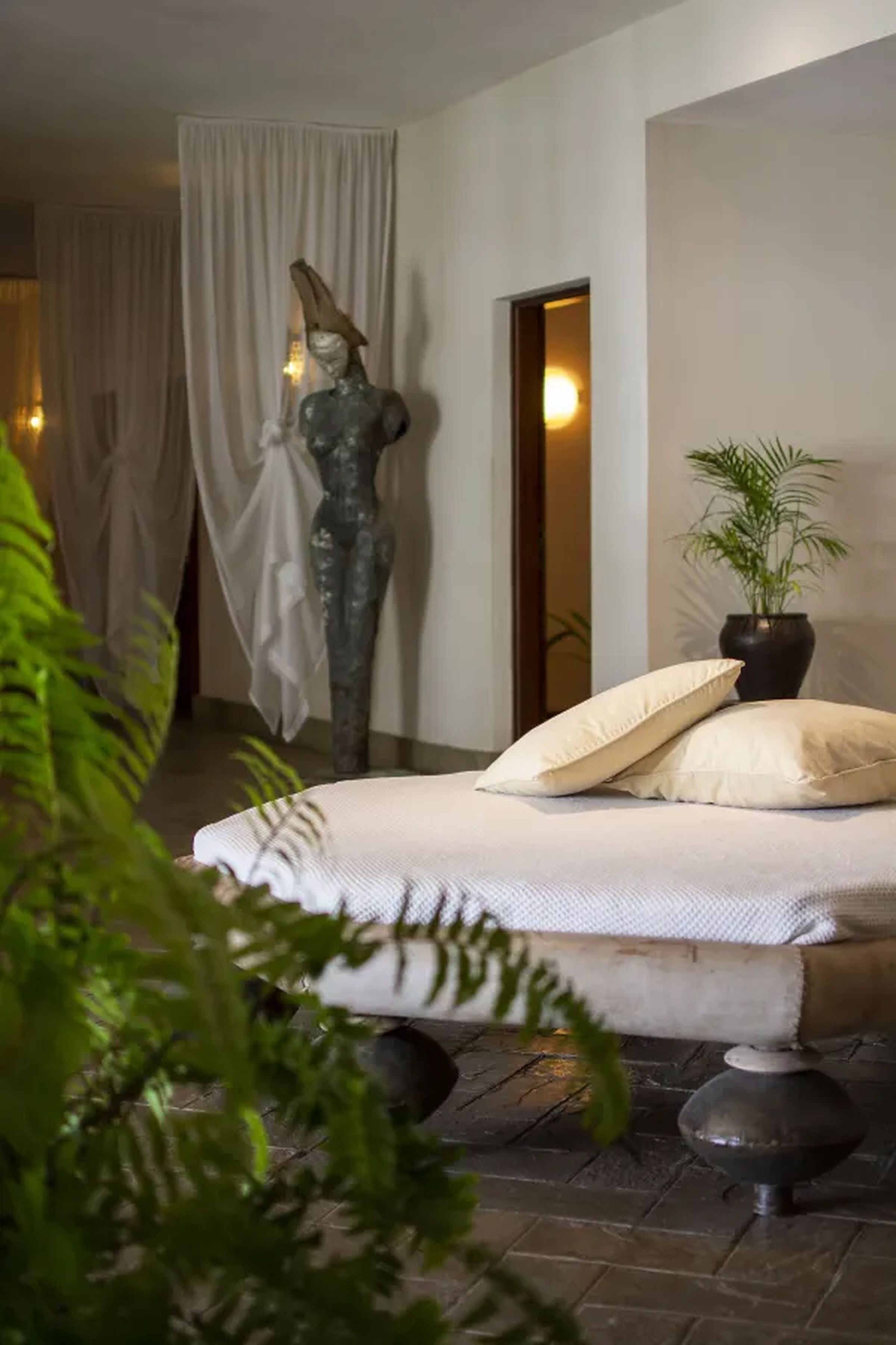 A bedroom with a bed, a potted plant, and a mannequin.