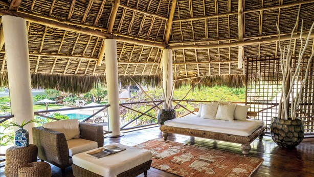 A spacious room with a thatched roof, wicker furniture, a large bed, and a view of a pool and greenery. - Lion in the Sun Boutique Hotel & Spa (Malindi)