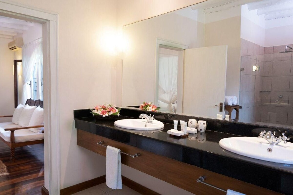 A bathroom with a large mirror, two sinks, a towel rack, and a wooden chair.