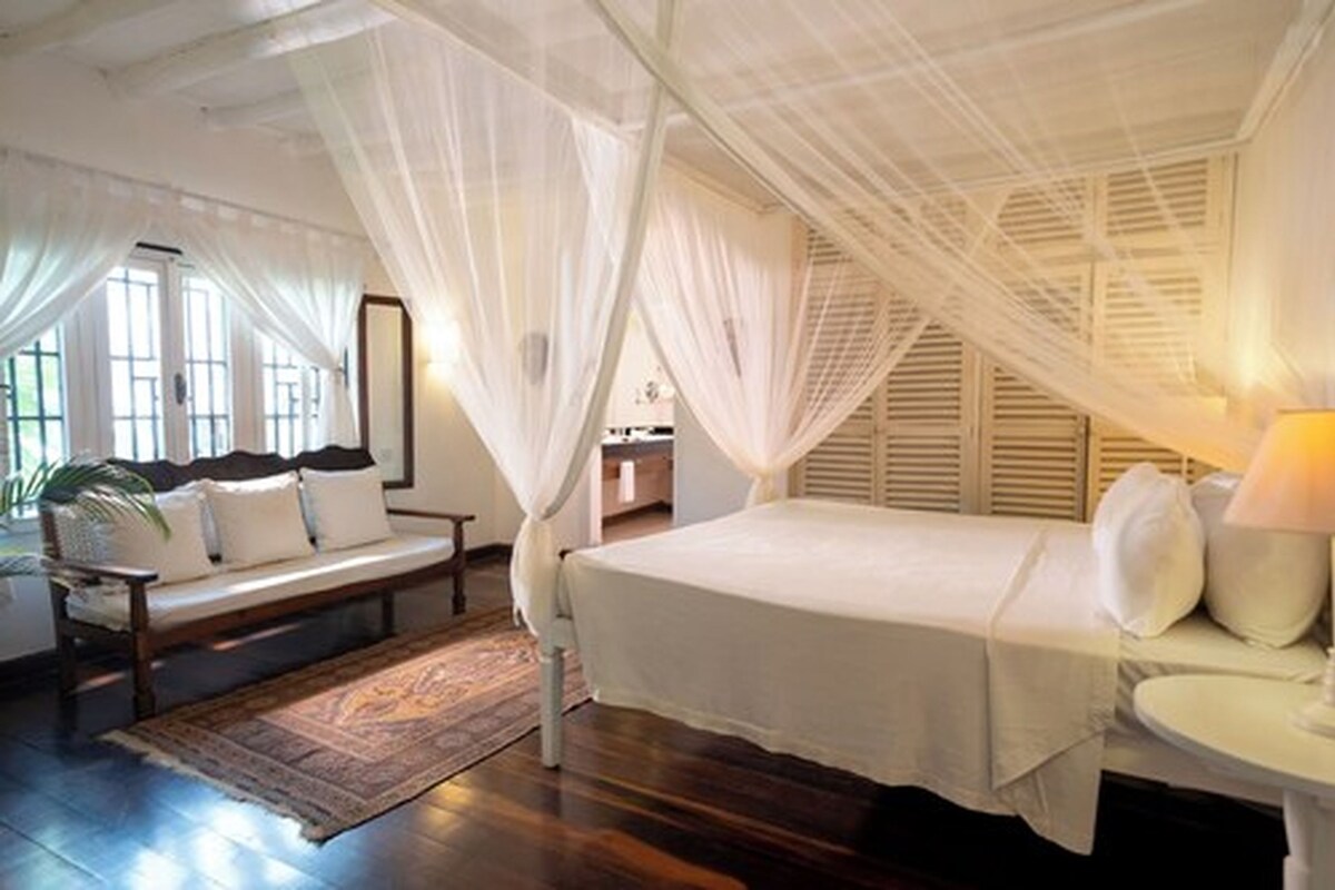 A bedroom with a canopy bed, a sofa, and a small table.