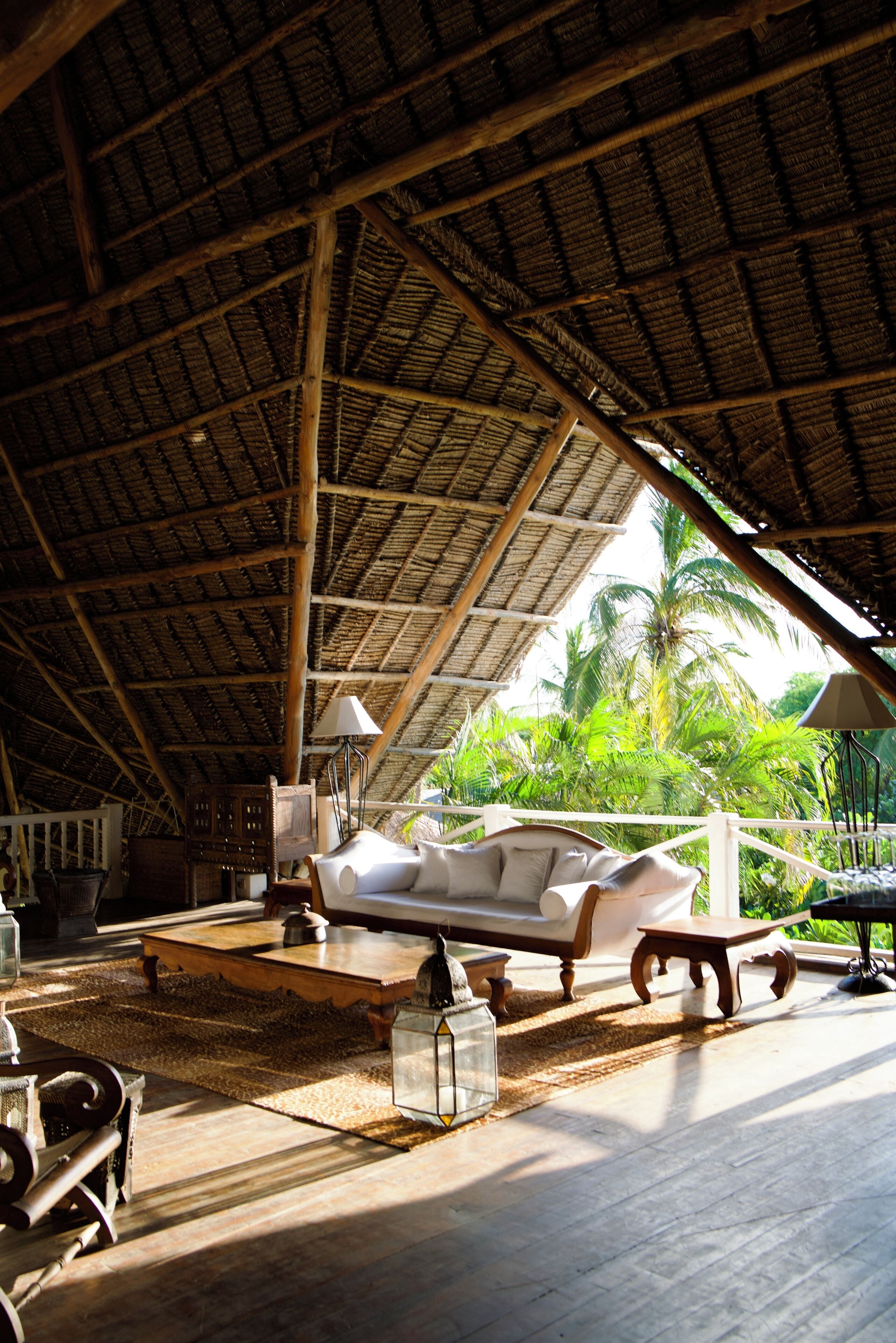 A room with a thatched roof, a white sofa, a wooden table, and a lamp.