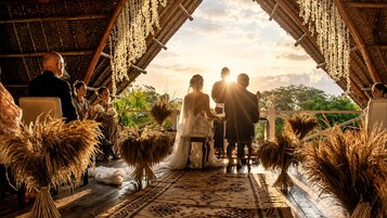 Una ceremonia de boda bajo un techo de paja, con invitados sentados a ambos lados.