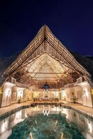 Una estructura amplia y abierta con techo de vidrio, piscina al frente y montañas como telón de fondo.