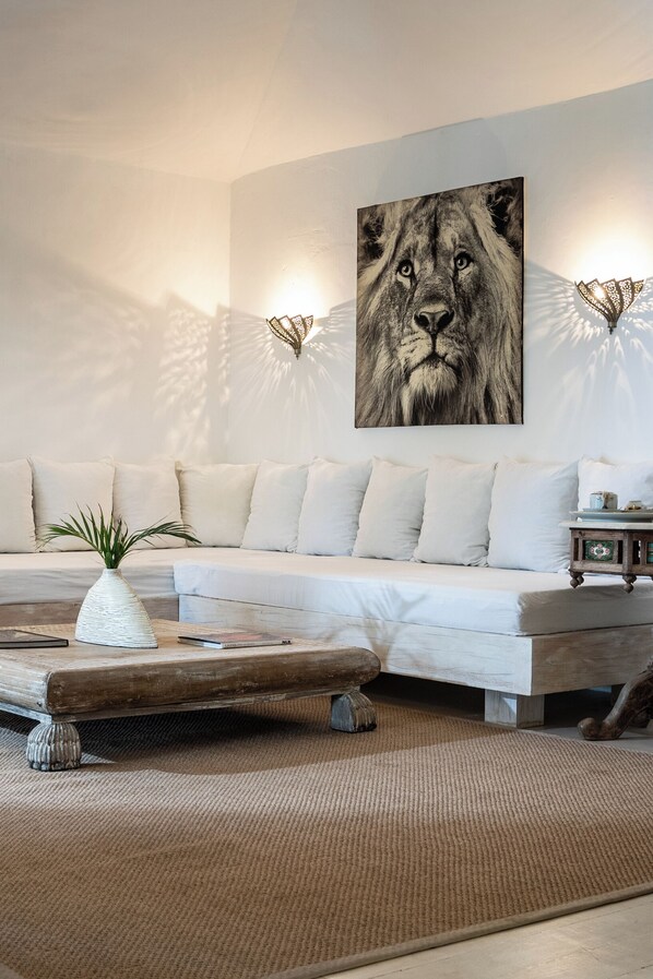 Un salon moderne avec un canapé blanc, une table basse en bois et une grande œuvre d’art encadrée représentant le visage d’un lion.