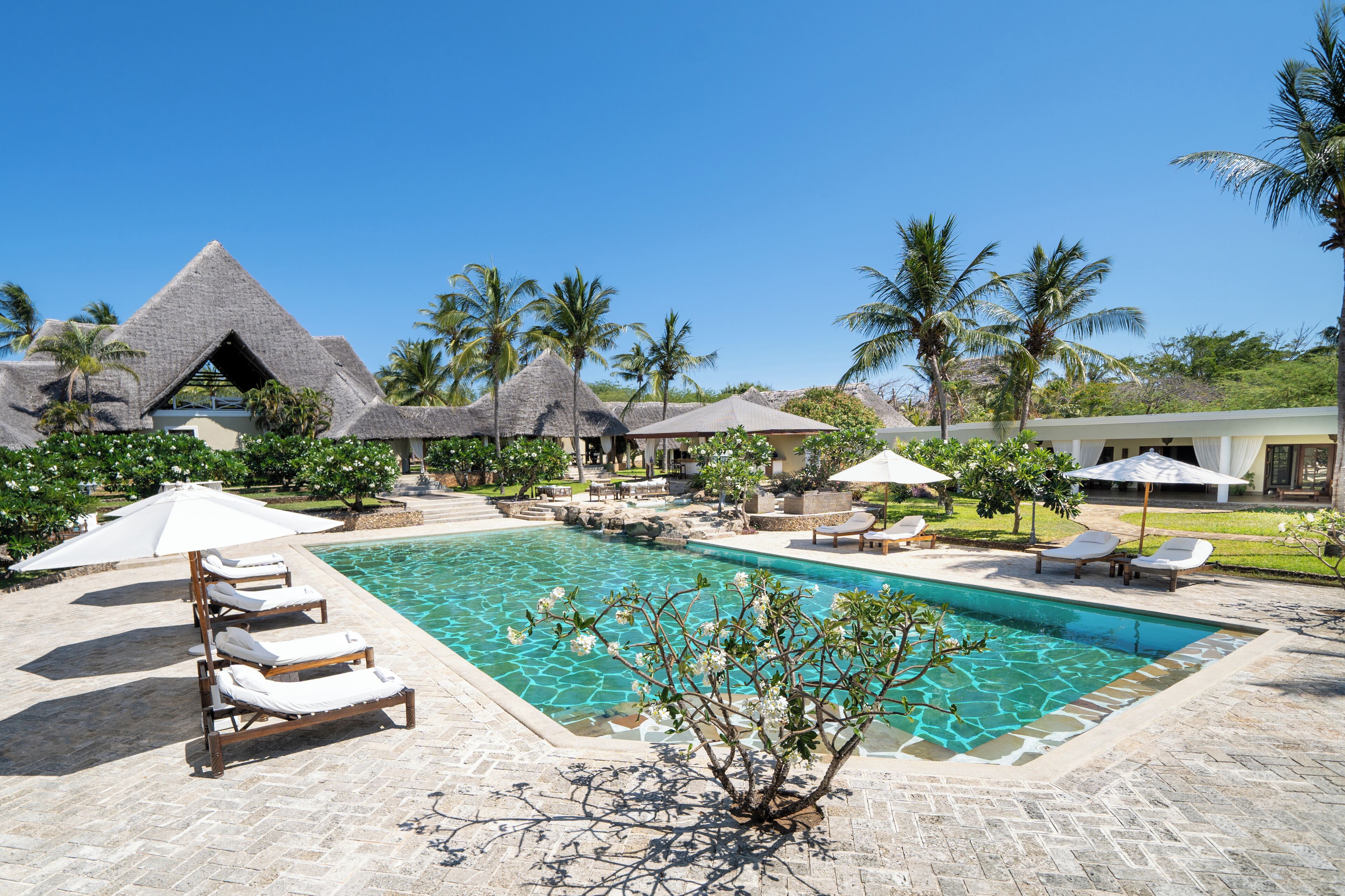 A pool area with lounge chairs, a clear pool, and thatched-roof structures.