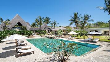 A pool area with lounge chairs, a clear pool, and thatched-roof structures.