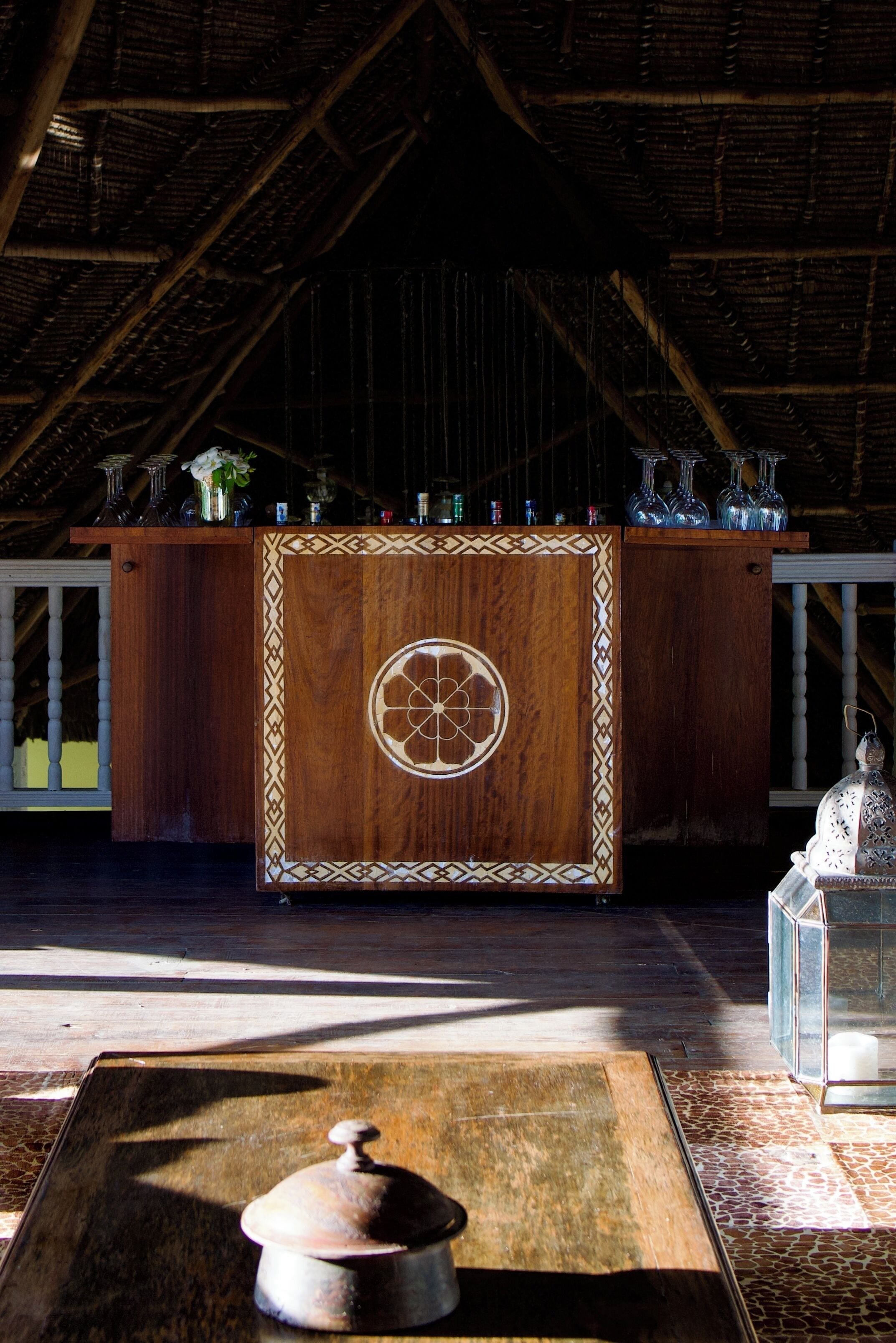 Un coin bar en bois avec un motif décoratif, un grand pot posé sur le sol et une lanterne sur la droite.