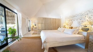 A spacious bedroom with a large bed, a decorative headboard, and a view through a sliding glass door.