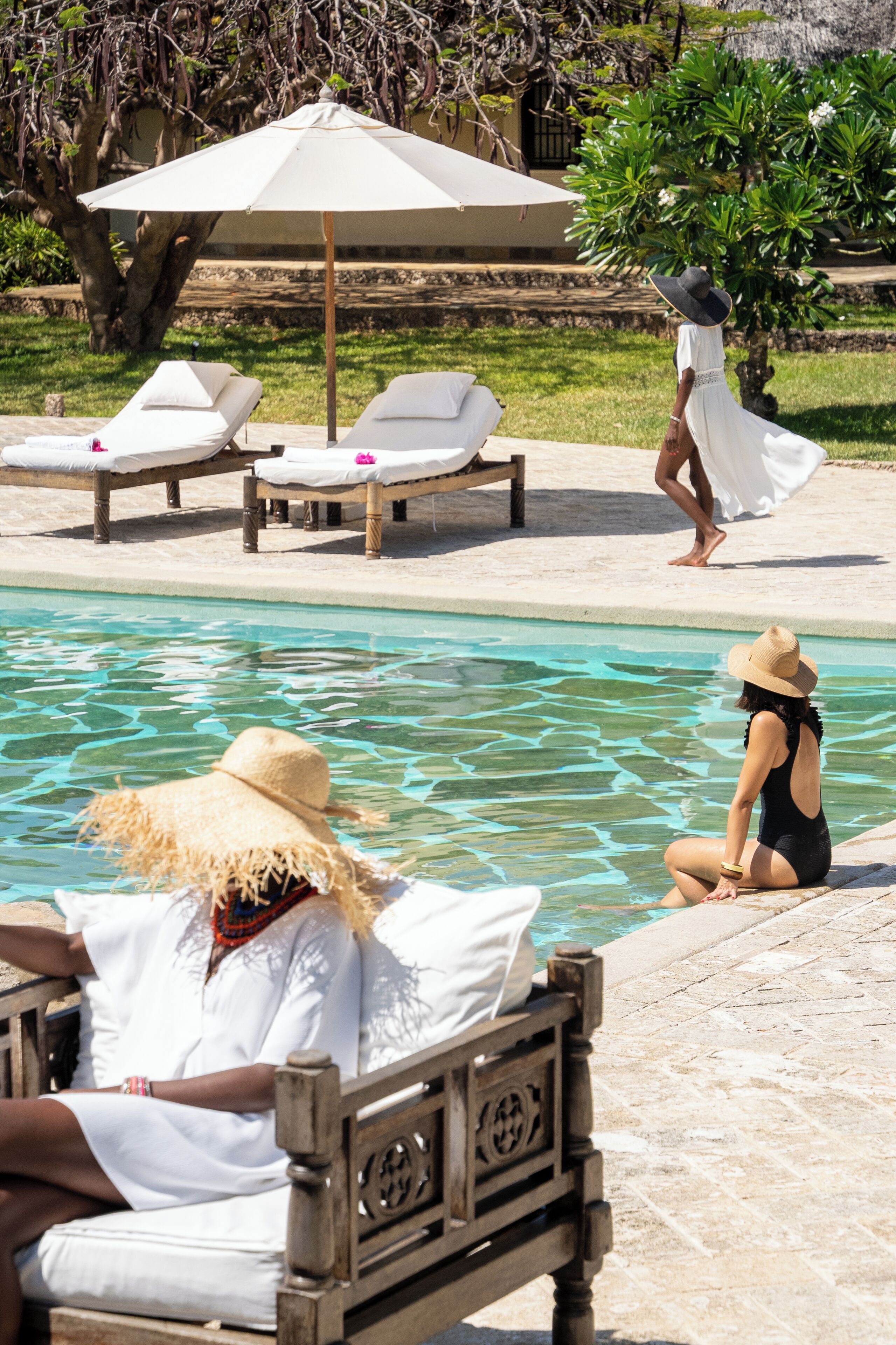 A pool area with lounge chairs, a wooden bench, and a person sitting by the pool.