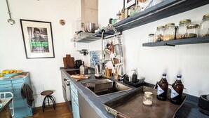 Eine Küche mit blauer Arbeitsplatte, einem Spülbecken und einem Wandregal mit Gläsern. Ein Stuhl und ein Tisch mit Zitronen sind ebenfalls vorhanden.