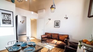 Eine moderne Küche mit Esstisch, Stühlen und einer Couch. Ein Kühlschrank, eine Hängeleuchte und ein gerahmtes Bild sind ebenfalls vorhanden.