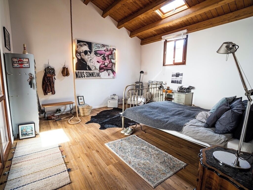 Et soveværelse med seng, skrivebord, stol, lampe og et vindue.
