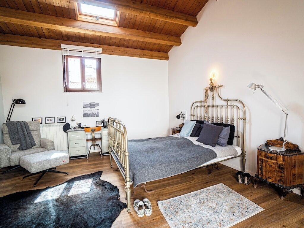 Een slaapkamer met een houten plafond, een metalen bed, een bureau en een stoel.
