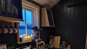 Eine kleine Küche mit einer Holzarbeitsplatte, einem integrierten Geschirrspüler und einem Fenster mit Blick auf eine verschneite Landschaft.