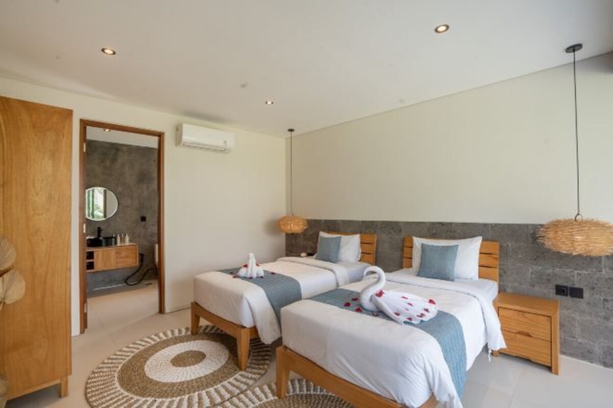 Un dormitorio moderno con dos camas, un armario de madera, un baño con espejo y una alfombra circular.
