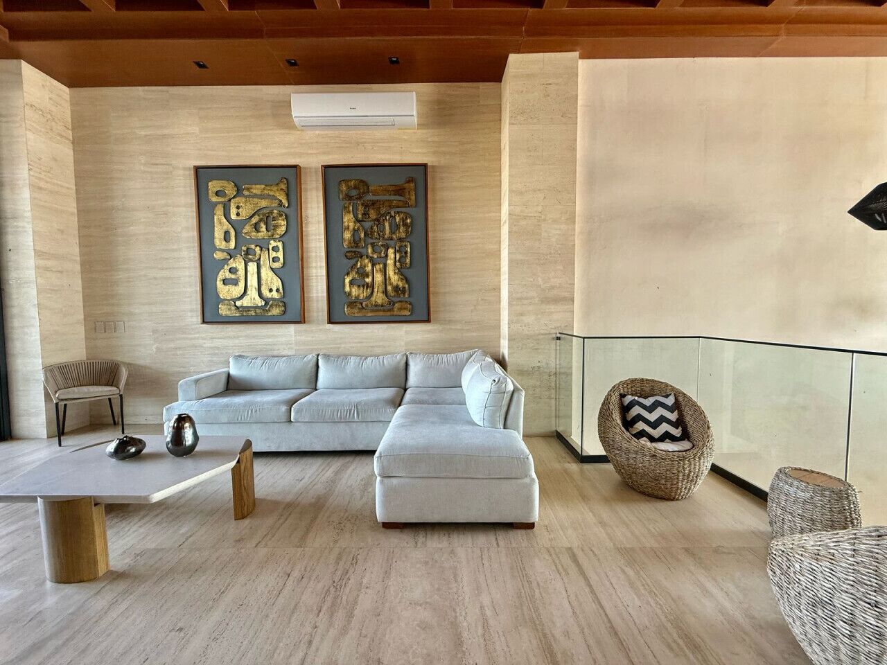 Ein modernes Wohnzimmer mit einem hellgrauen Ecksofa, einem Holztisch und zwei abstrakten goldenen Bildern an der Wand.
