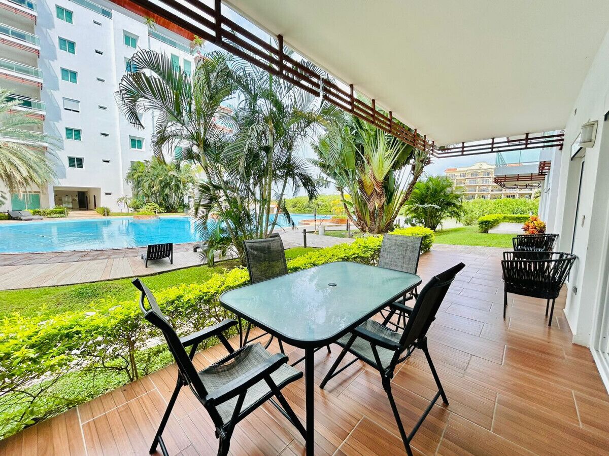 Un espace extérieur abrité, doté d’une table et de chaises, d’une piscine et offrant une vue sur un bâtiment en arrière-plan.