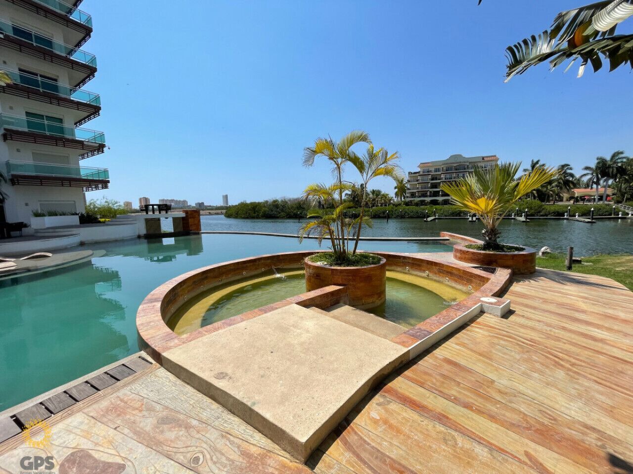 A pool area with a wooden deck, a circular hot tub, and potted plants.