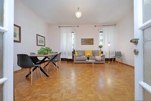 A spacious living room with a wooden parquet floor, a sofa with yellow cushions, a dining table with chairs, and a chandelier. - 4bnb - Corridoni Apartment (Rome)