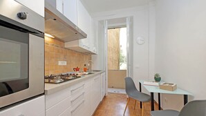 A compact kitchen with white cabinets, a gas stove, and a small dining area with two chairs and a table. - 4bnb - Corridoni Apartment (Rome)