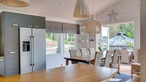 A modern kitchen with a large wooden table and wicker chairs, a built-in fridge, and pendant lights. - Luxury villa by the sea, Kustavi (Varsinais-Suomi)