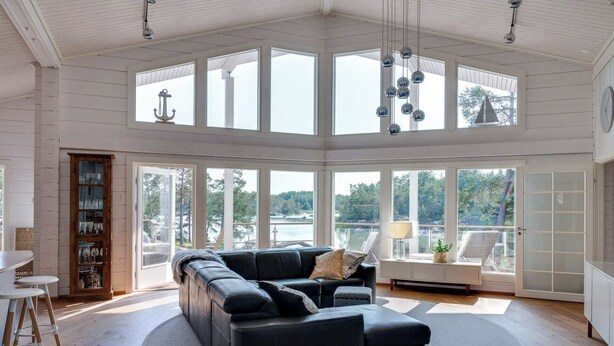 A spacious living room with a large black sectional sofa, a round coffee table, and a view of a lake through large windows. - Luxury villa by the sea, Kustavi (Varsinais-Suomi)