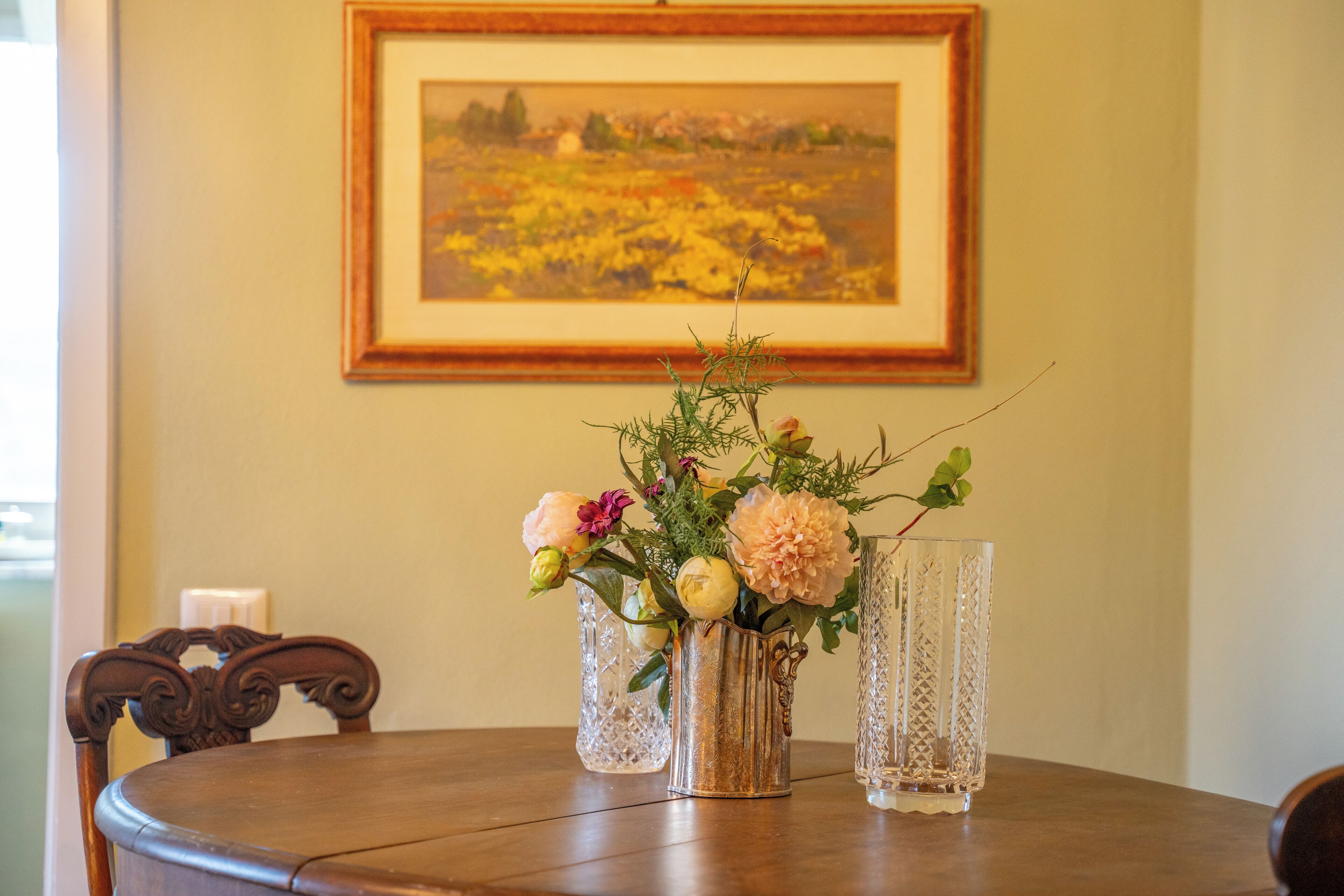 A dining table with a vase of flowers and two clear glass vases.