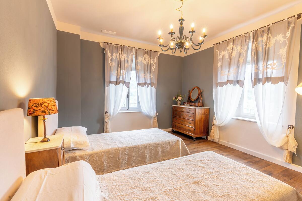 Ein Schlafzimmer mit zwei Betten, einem Schminktisch, einer Chandelüster und Vorhängen.