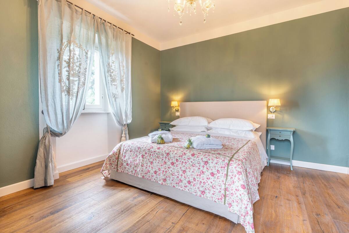 Ein Schlafzimmer mit Bett, Vorhängen, einem Nachttisch und einer Wandlampe.