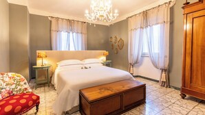 Une chambre à coucher avec un grand lit, un banc en bois, une table de chevet avec une lampe et un lustre.