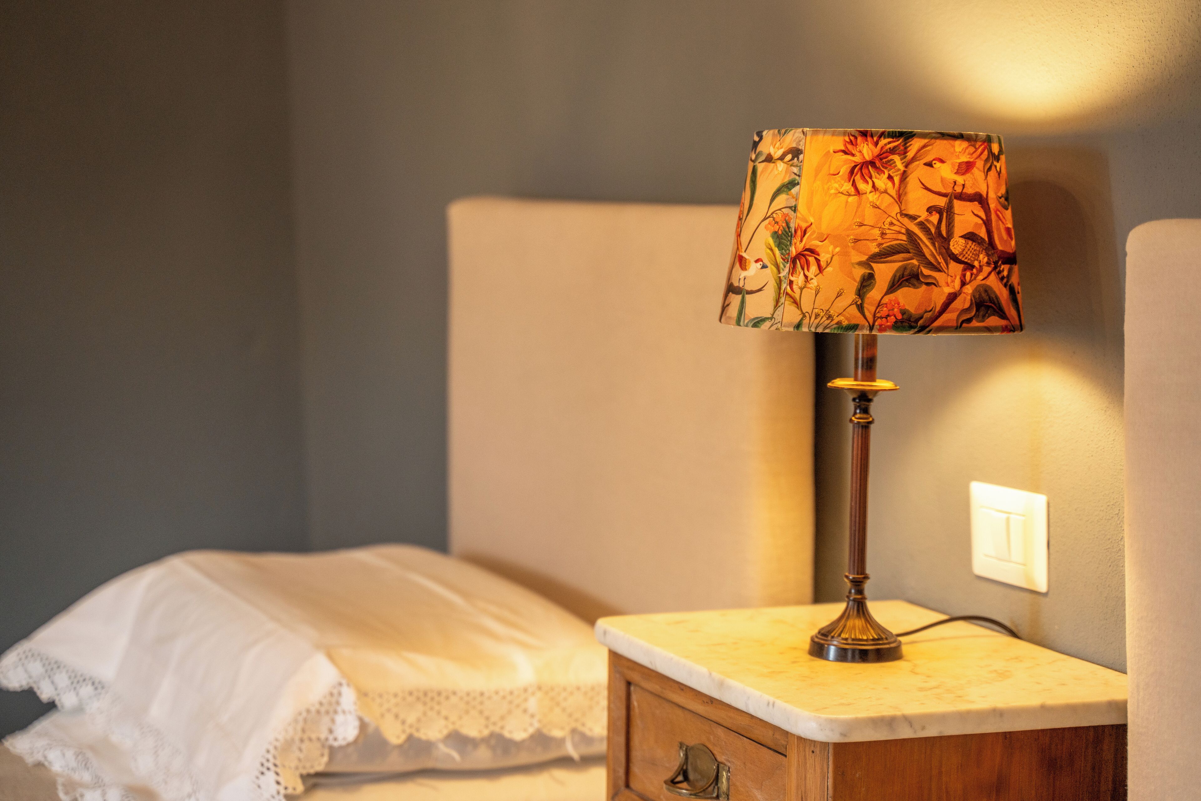 A bedside table with a lamp, a bed with a white blanket, and a nightstand.